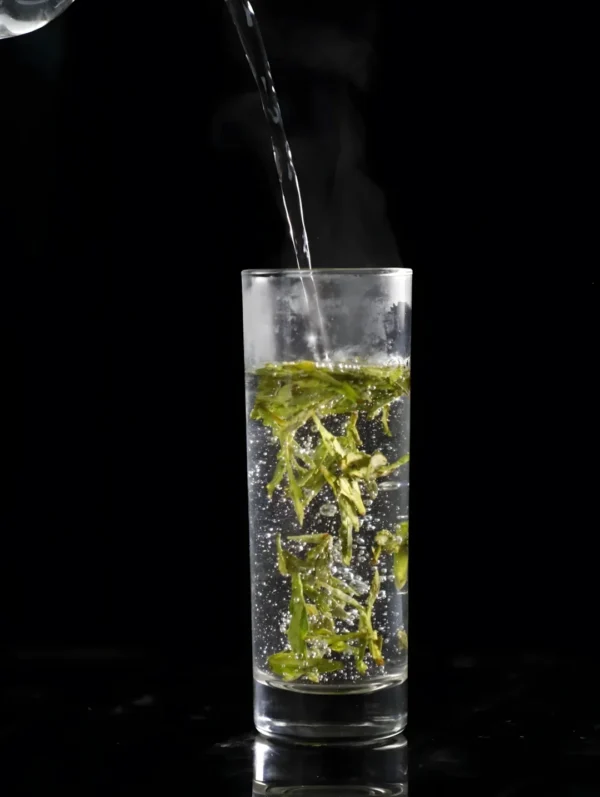 Hot water being poured into a glass of loose leaf green tea, showcasing hangzhou dragon well tea, slim tea, and skinny tummy tea benefits.