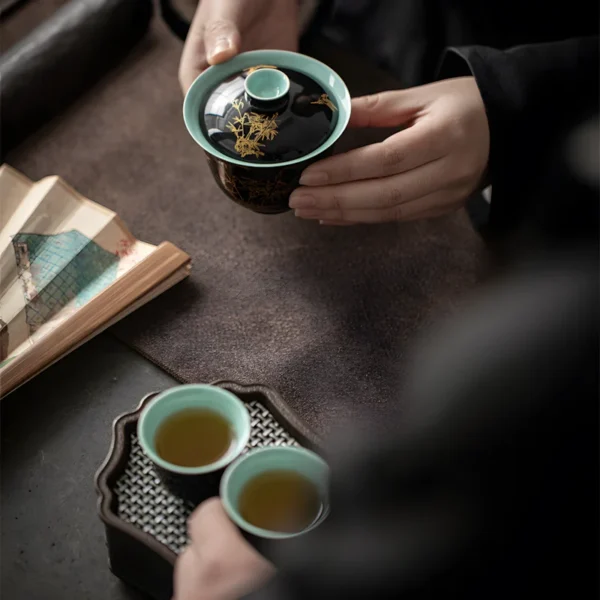 A person holding an antique ceramic tea set piece with painted details, part of a polish ceramic tea mug set on a tea table.