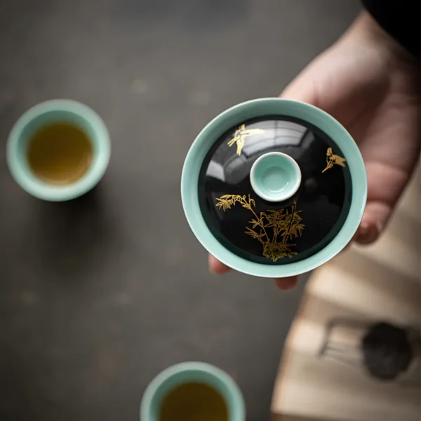 A porcelain ceramic gaiwan with gold bamboo patterns, part of a green ceramic tea set, accompanied by porcelain ceramic tea cups.