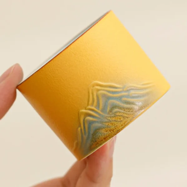 Handcrafted ceramic tea cup showcasing intricate mountain-inspired textures and vibrant yellow color, perfect for tea enthusiasts.