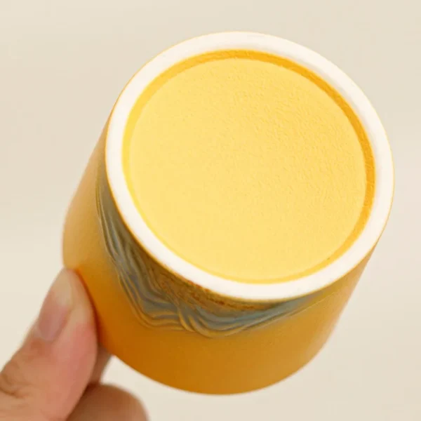 Base of a yellow ceramic tea cup featuring textured mountain patterns, handcrafted details, and a vibrant finish.