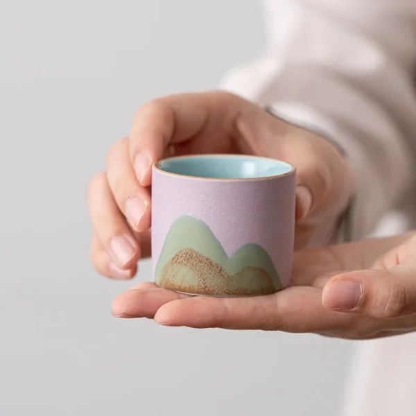 A small, handcrafted ceramic cup featuring pastel-colored mountain motifs, perfect for tea enthusiasts and collectors.