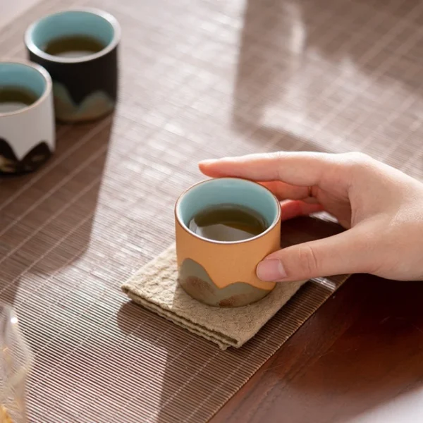 A minimalist ceramic tea cup with an earth-toned mountain pattern, placed on a mat, perfect for enjoying hot beverages.