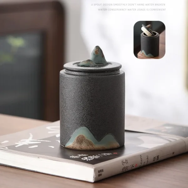 Handcrafted ceramic tea canister featuring a lid and mountain motif, complements ceramic tea strainers and teapot sets.