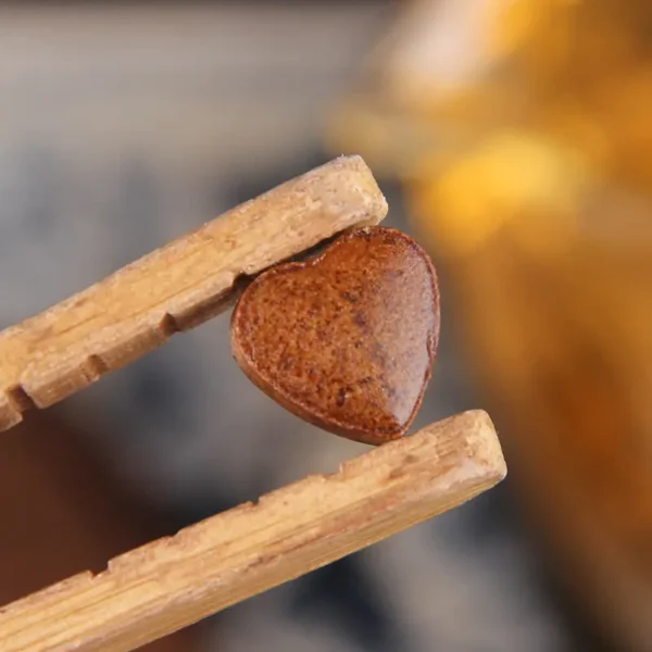 Heart-shaped jasmine Pu'er tea paste delicately held with wooden chopsticks, showcasing premium craftsmanship and natural ingredients.