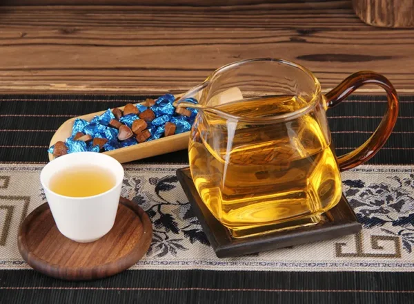 A warm brew of jasmine Pu'er tea paste with golden tea liquor in a glass teapot, paired with individually wrapped heart-shaped tea paste.
